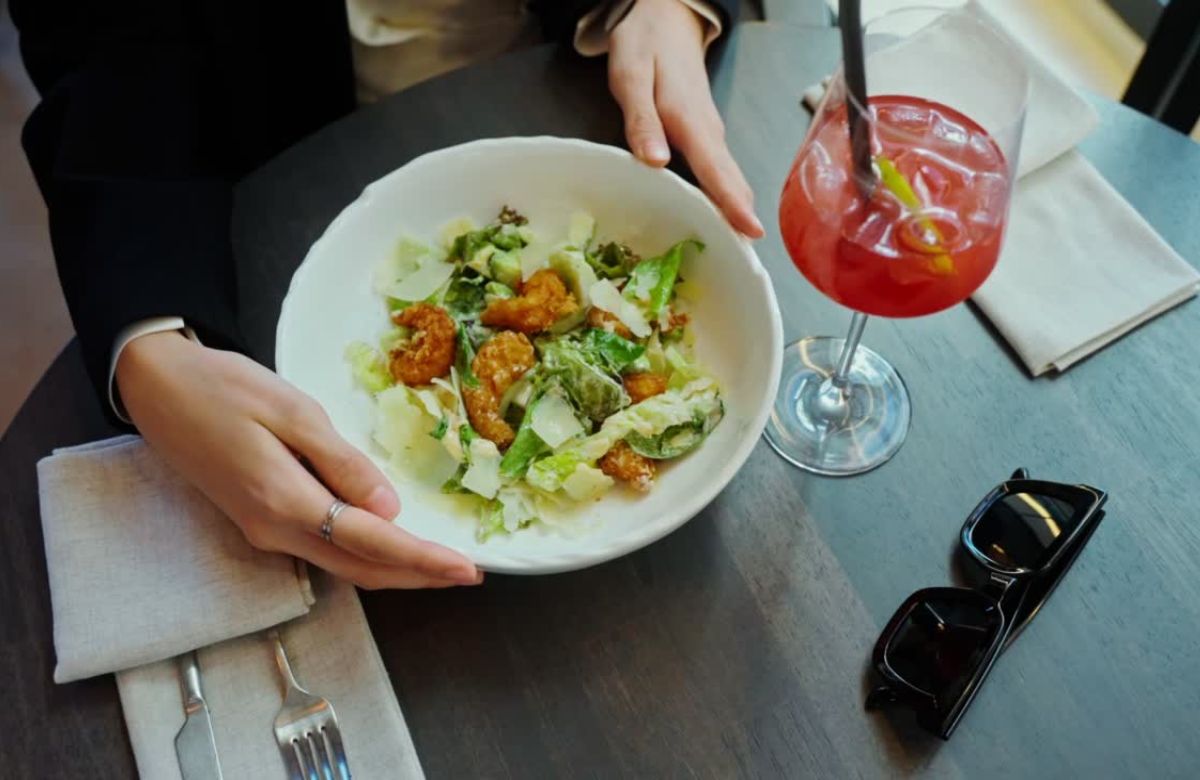 Devojka sedi u restoranu, salata sa gamborim i rozi koktel na stolu