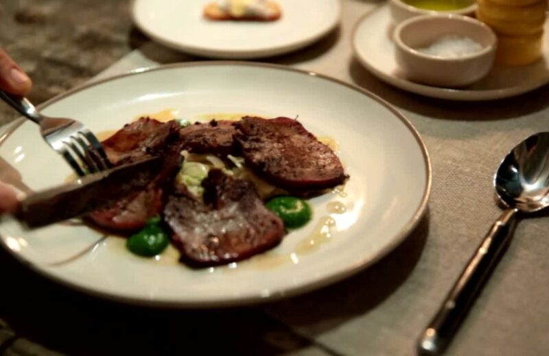 Muškarac ruča u rastoranu, drži viljusku i nož u rukama a na tanjiru su posluženi komadi steak mesa.